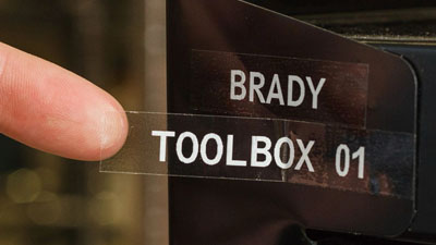 Een transparant label met de witte tekst Brady toolbox 01 aangebracht op een stuk metaal.