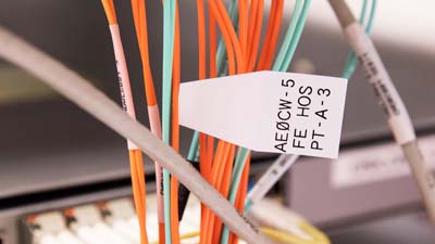 Een QuickFlag-label van Brady dat aan een kabel is bevestigd, tussen een grotere groep labels, met bedrukking om deze te identificeren.