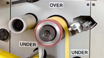 Verschillende weerbestendige vinyllabels van Brady met de tekst OVER en UNDER aangebracht op een stansmachine om aan te geven in welke richting het materiaal moet worden ingeregen.