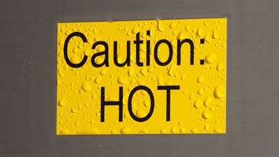 Een geel Brady ToughWash-label met de tekst CAUTION HOT erop geprint. Het label is nat alsof het onlangs is schoongespoten.