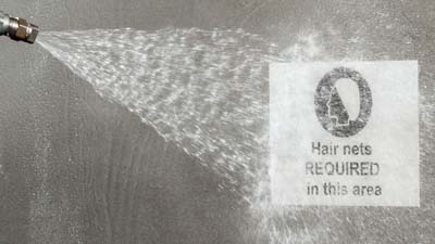 Een werknemer gebruikt een hogedrukspuit om een metaaldetecteerbaar ToughWash-label van Brady te reinigen dat op een machine is aangebracht.