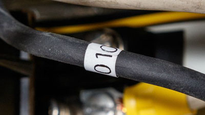 Een wit zelfdovend Tedlar-wikkellabel met zwarte tekst aangebracht rond een zwarte draad van een elektriciteitskast.